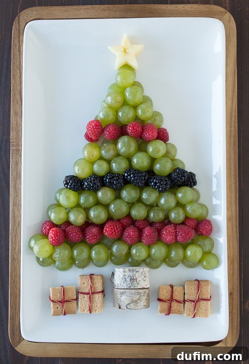 Overhead shot of the Christmas tree fruit platter, showcasing the arrangement of grapes, raspberries, blackberries, apple star, graham cracker presents, and a simple tree trunk.
