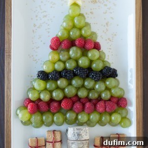 A festive Christmas tree fruit platter made with an apple star, grapes, raspberries, blackberries, and graham cracker presents, perfect for a healthy holiday treat.