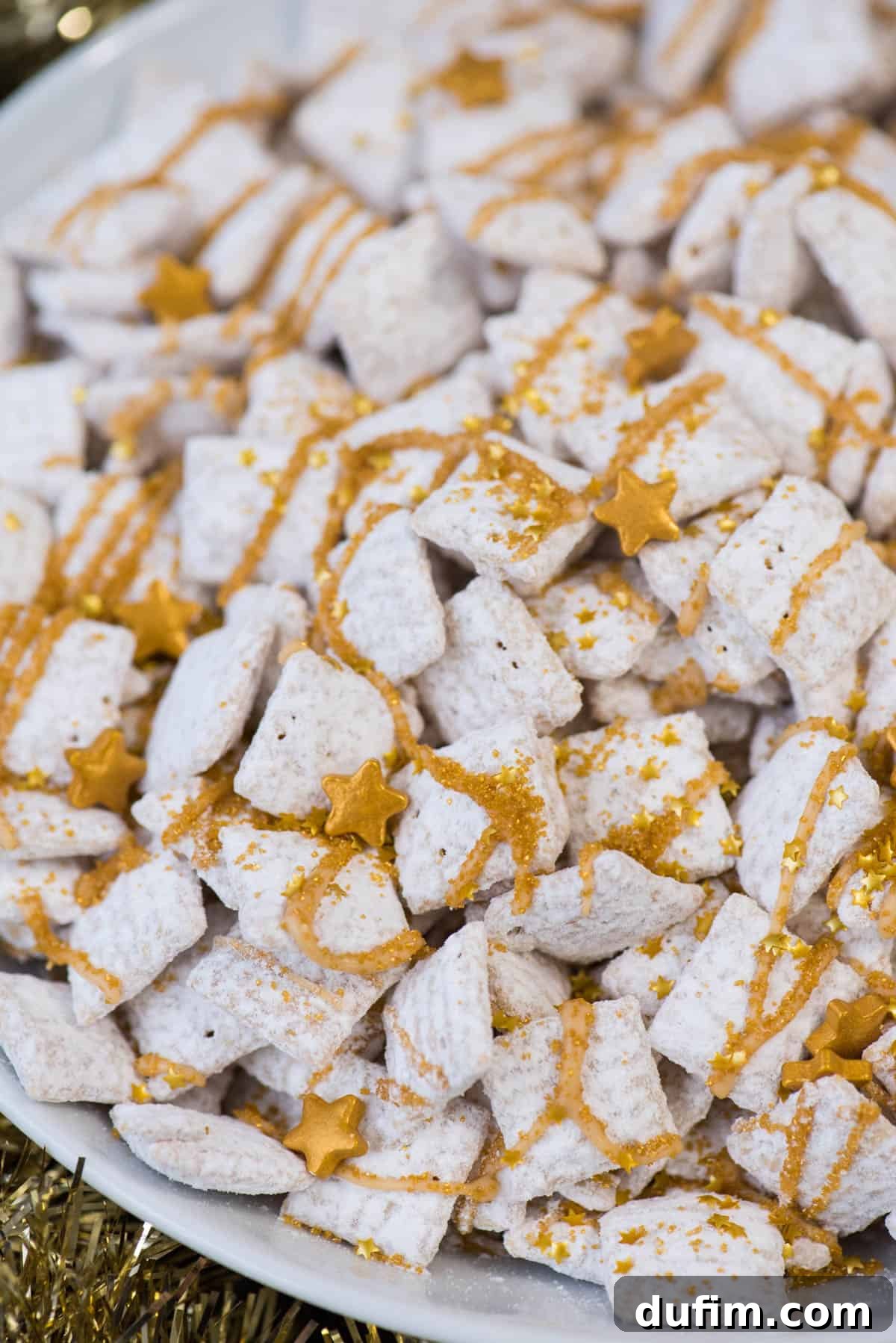 Sparkling White Chocolate New Year's Chow 6 A white bowl filled with New Year's Eve white chocolate puppy chow, generously garnished with gold sprinkles and gold stars, ready to be served at a festive gathering.