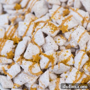 Sparkling White Chocolate New Year's Chow 8 A plate of new years eve puppy chow, coated in powdered sugar, drizzled with gold-colored icing, and topped with small gold star-shaped sprinkles, symbolizing a festive treat.