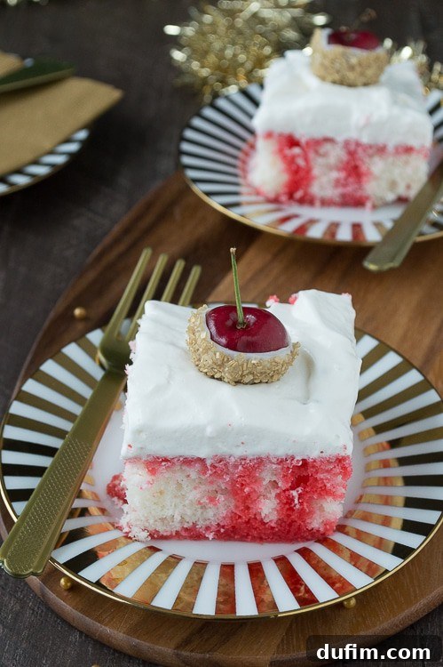 A slice of Champagne Cherry Poke Cake on a plate, showing the distinct layers of white cake and red cherry infusion, topped with whipped cream and a gold glitter cherry.