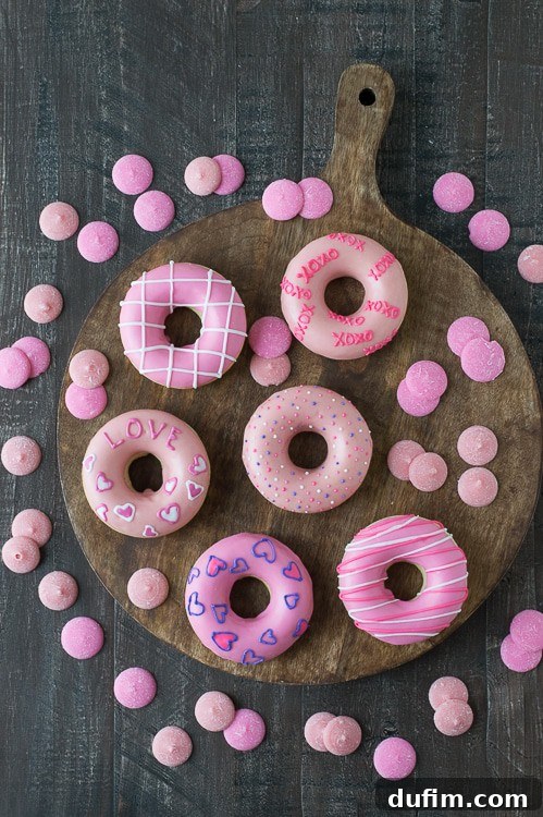 Delicious and cute Pink Valentine’s Day Donuts on a wooden board surrounded by pink candy melts, ready to be enjoyed.
