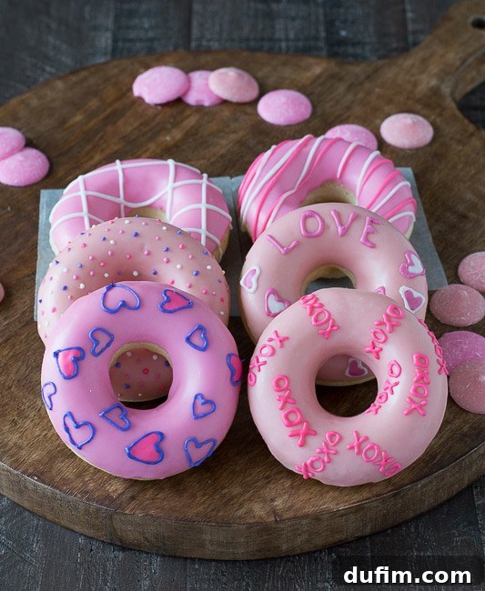 Six beautifully decorated Valentine’s Day Donuts covered in vibrant pink frosting on a rustic wooden board, a perfect romantic dessert.