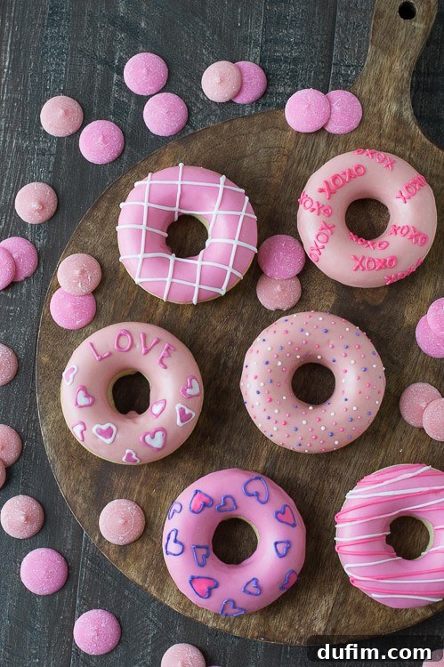 Six enchanting pink Valentine’s Day Donuts artfully arranged on a wooden board, surrounded by complementary pink candy melts, on a charming wooden table.