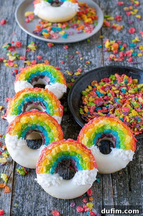 Vibrant Rainbow Donuts adorned with white chocolate glaze, colorful fruity pebbles, and fluffy shredded coconut, artfully arranged on a rustic wooden table.