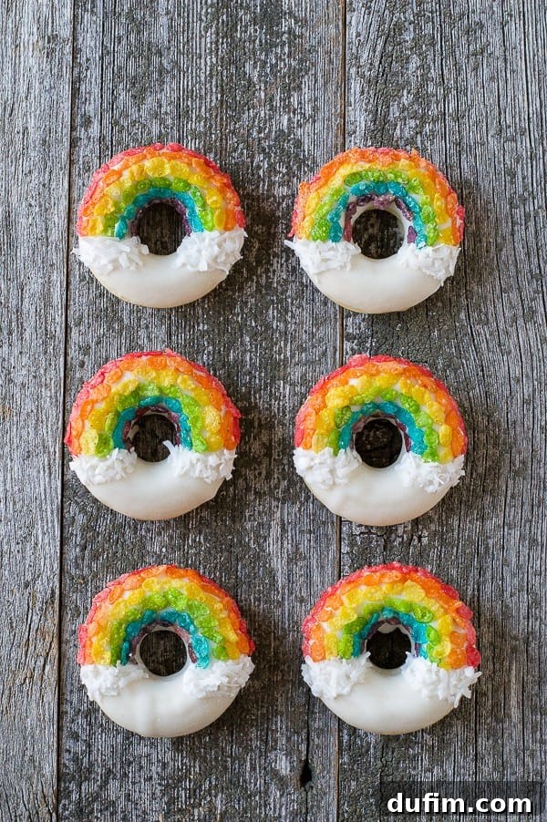 Six perfectly arranged homemade Rainbow Donuts on a rustic wooden surface, highlighting the vibrant cereal and pristine white glaze.