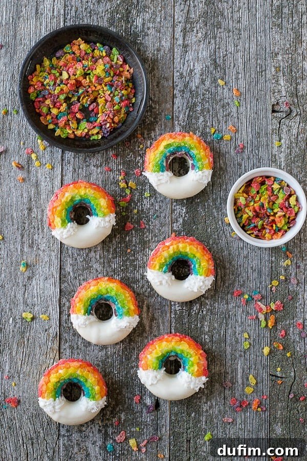 Six exquisitely decorated Rainbow Donuts, flanked by two bowls brimming with sorted Fruity Pebbles, all resting on a charming wooden table.