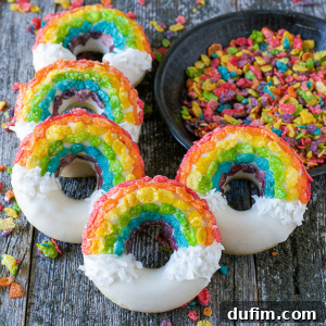 Five rainbow donuts decorated with rainbow-colored cereal and white icing resembling clouds are arranged on a rustic wooden surface, with a bowl of colorful cereal pieces nearby.
