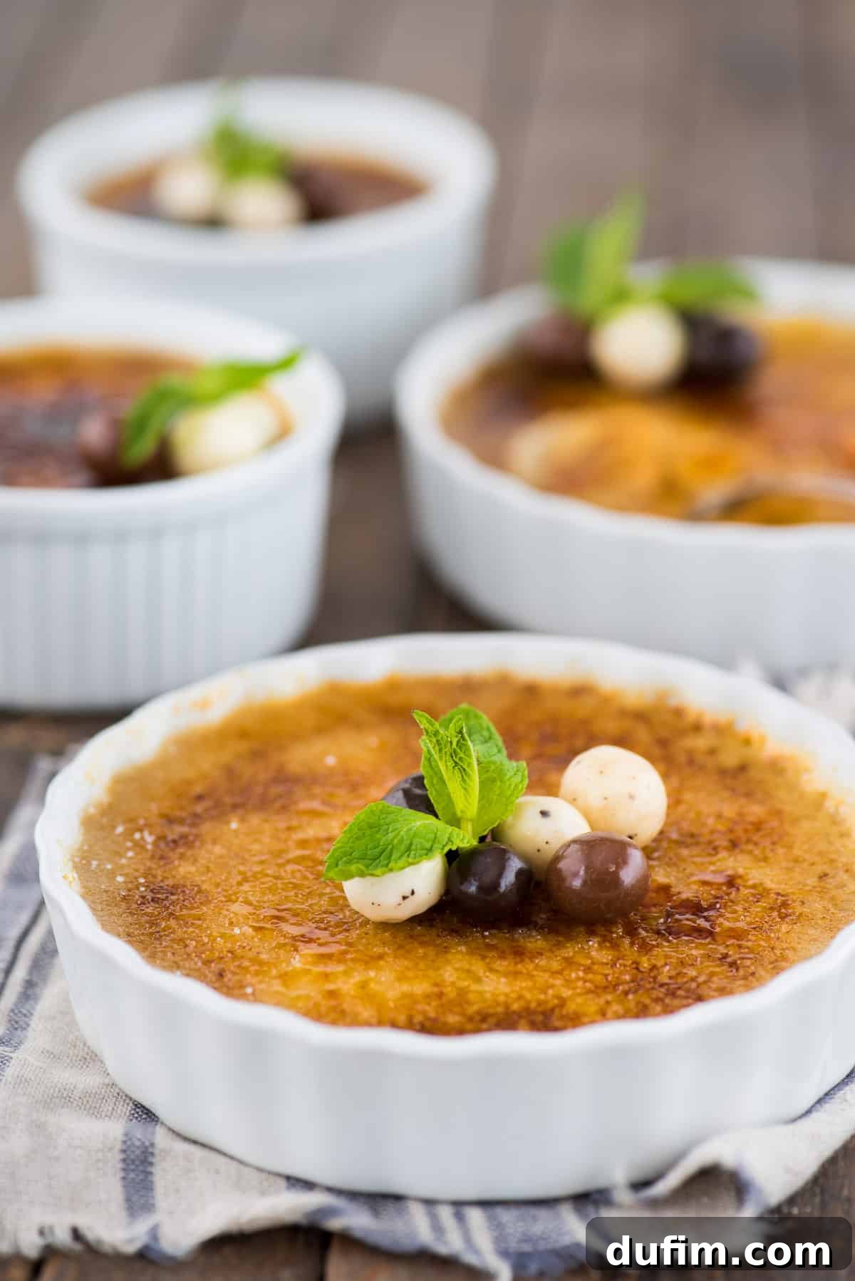 Exquisite espresso crème brûlée served in a white round ramekin, garnished with rich chocolate-covered coffee beans and a fresh mint leaf, set against an elegant backdrop.