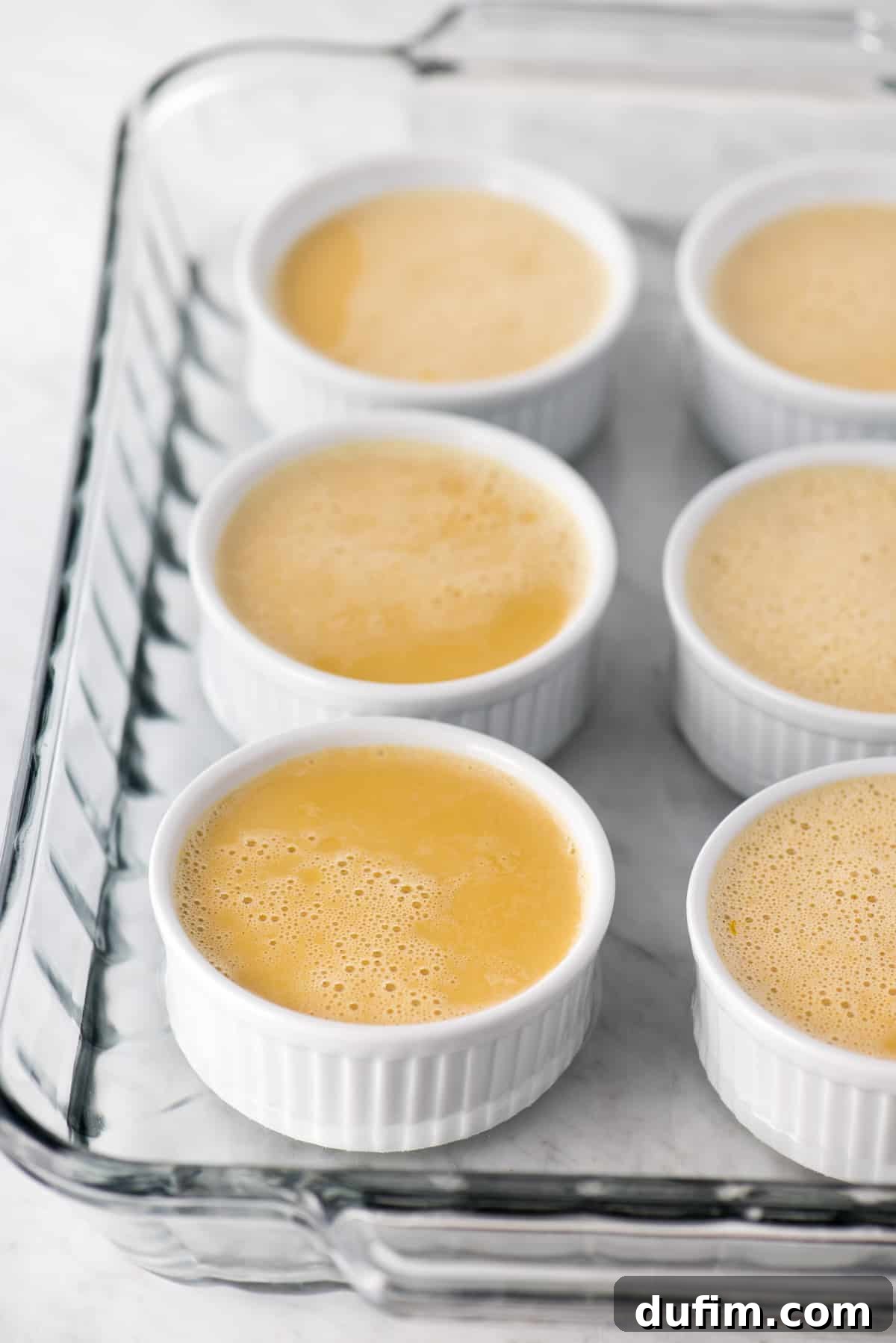 A beautifully presented espresso crème brûlée in a white ramekin, adorned with delicate chocolate-covered coffee beans and a sprig of fresh mint, creating an inviting visual treat.