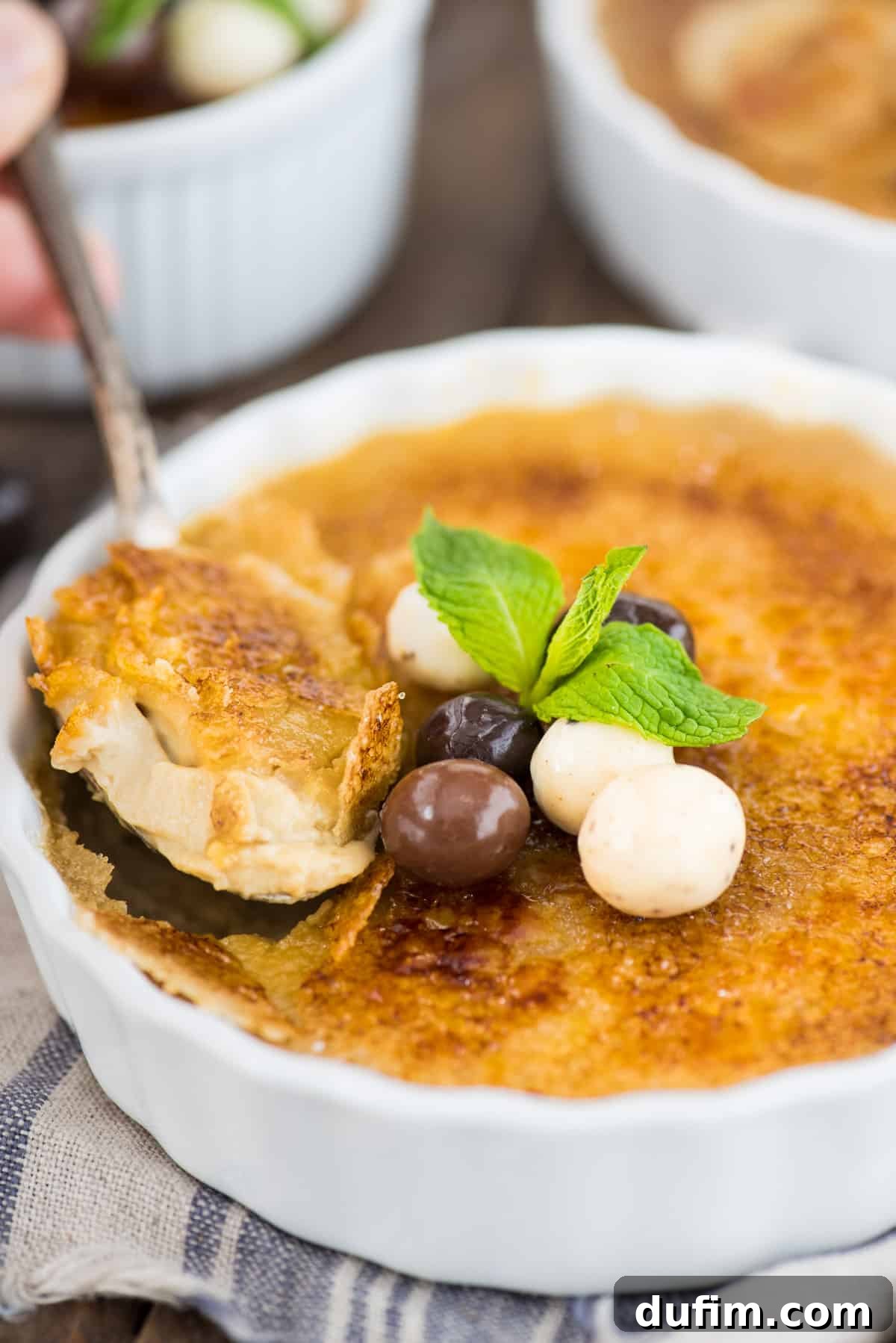 A pristine white round ramekin holding creamy espresso crème brûlée, artfully garnished with chocolate-covered coffee beans and a fresh mint leaf, ready to be enjoyed.