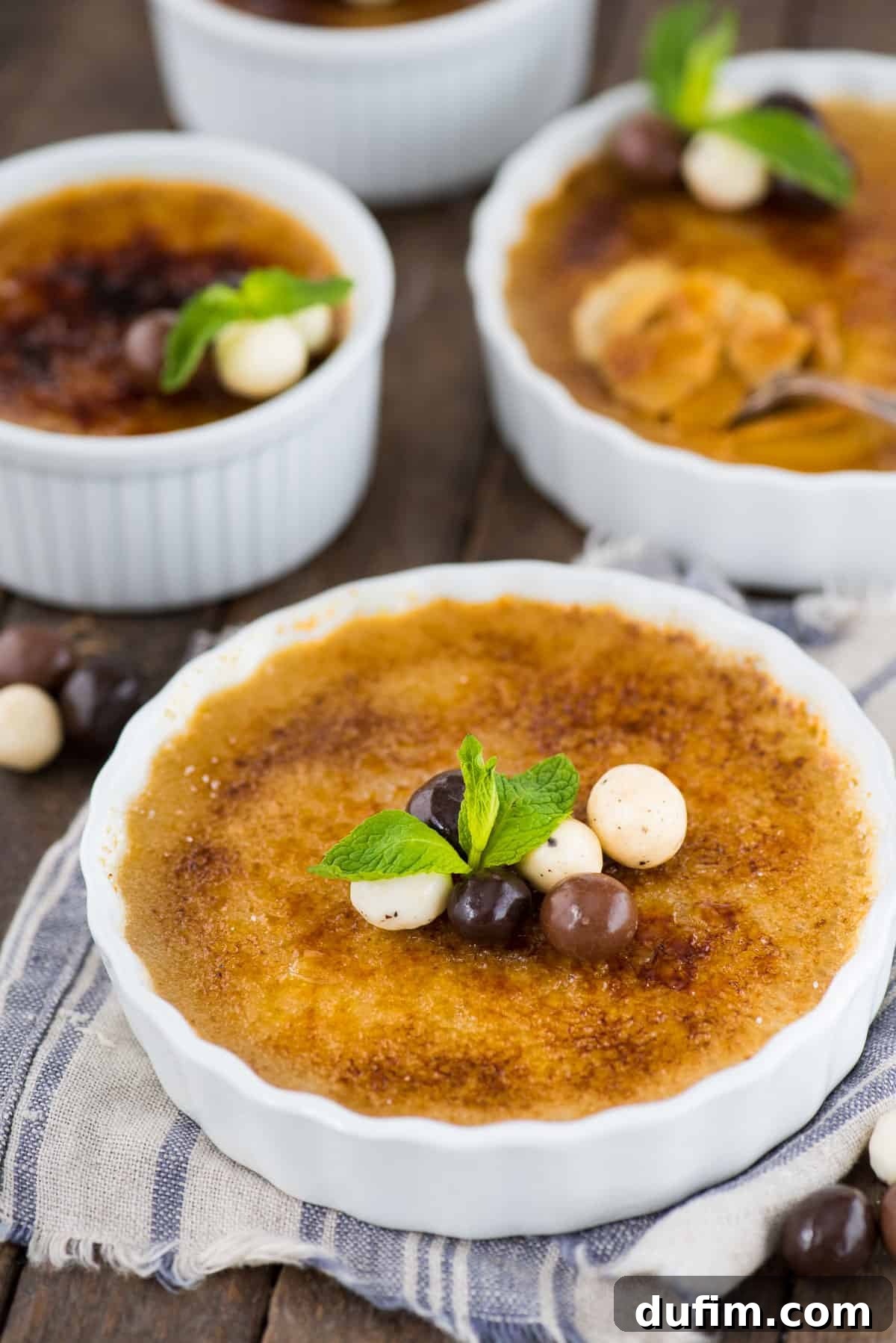 A delectable espresso crème brûlée in a white ramekin, adorned with chocolate-covered coffee beans and a fresh mint leaf, perfectly prepared and ready for a special occasion.