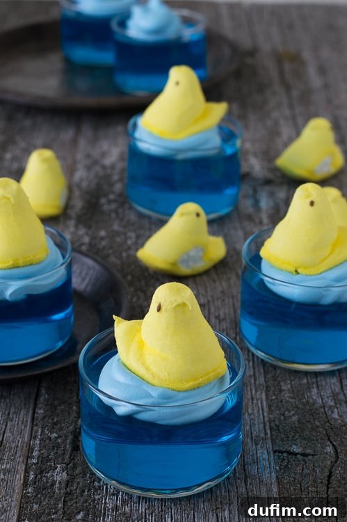 Vibrant blue jello in a clear glass bowl, topped with a bright yellow marshmallow Peep chick, ready for an Easter celebration.