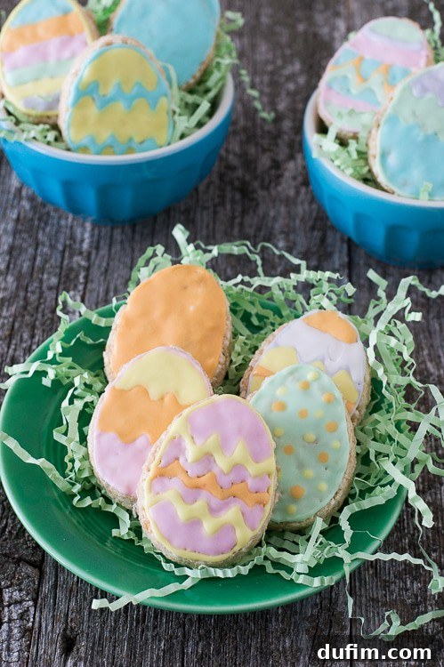 Five Rice Krispies Easter Eggs on fake green grass on a green plate on a wooden table, beautifully decorated with pastel royal icing.