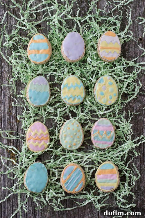 Twelve Rice Krispies Easter Egg treats displayed on fake green grass on a rustic wooden table, showcasing their vibrant decorations.