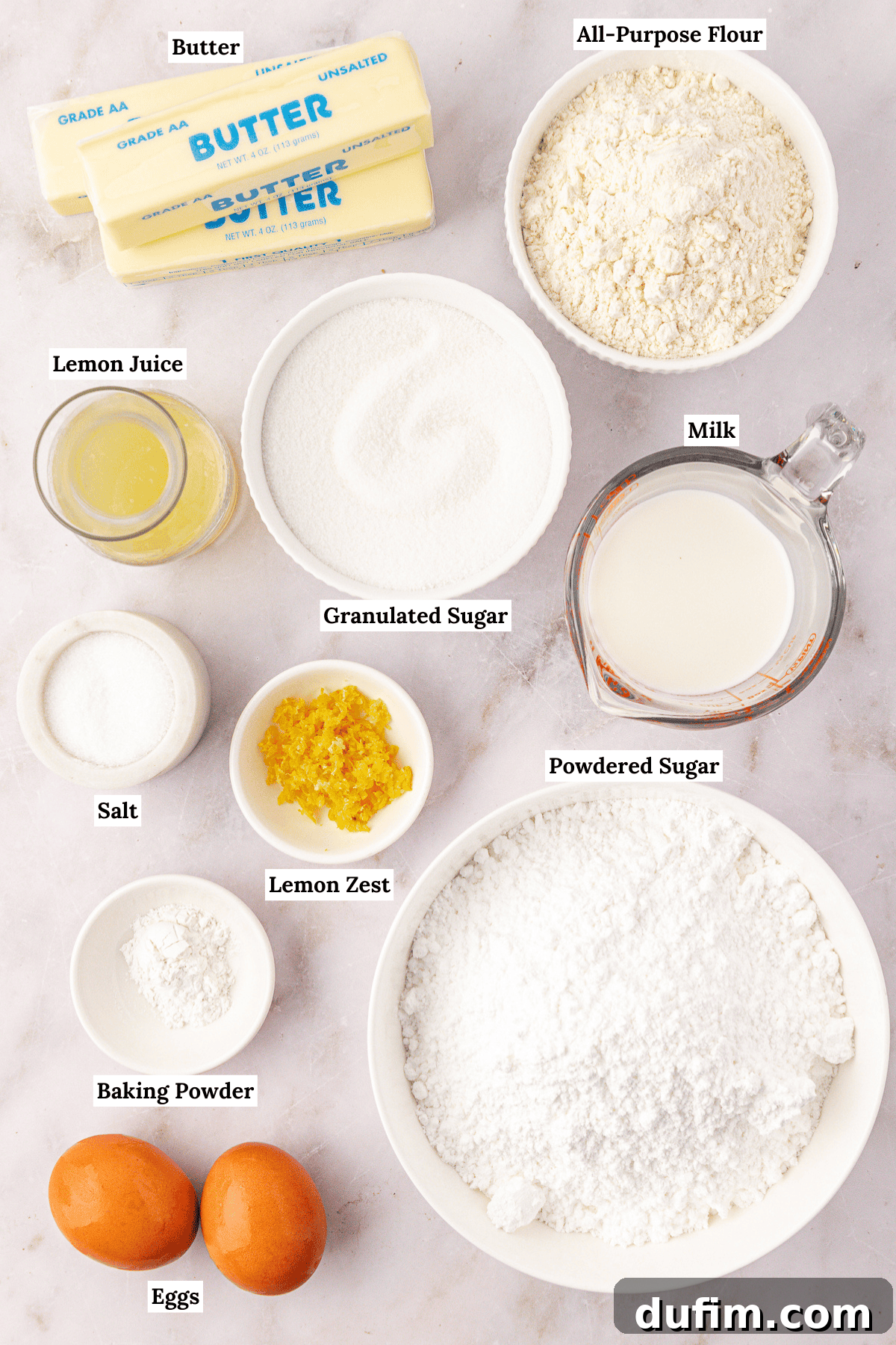 Top-down view of baking ingredients including butter, all-purpose flour, granulated sugar, milk, powdered sugar, eggs, baking powder, salt, lemon zest, and lemon juice, each labeled with text.