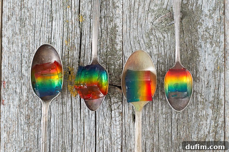 A close-up of a plate with several vibrant Rainbow Jello squares, highlighting the distinct colorful layers, with a fork poised to take a bite.
