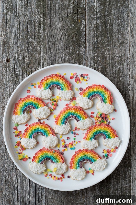 Rainbow Sugar Cookies - use fruity pebbles and shredded coconut to make these delicious rainbow cookies! Assortment of Eight delicious Rainbow Sugar Cookies on a large white serving plate on a wooden table.