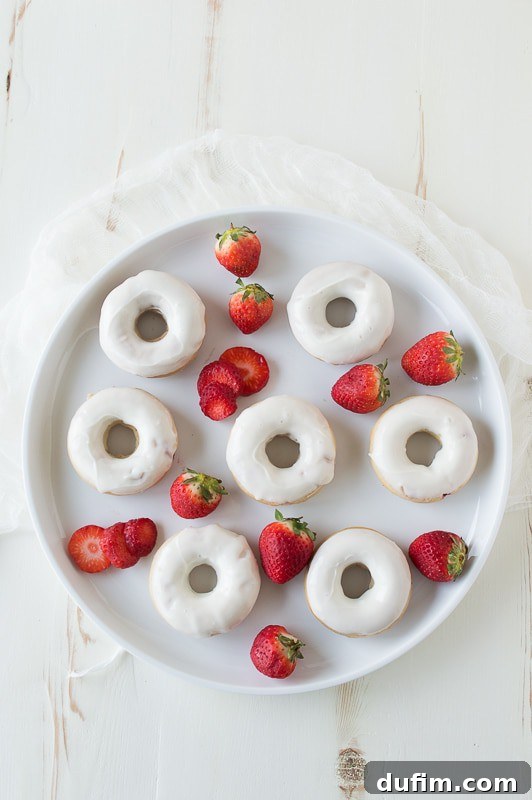 Strawberry Cheesecake Donut Delights 3 Close-up shot of a Strawberry Cheesecake Donut on a wire rack, showcasing the thick cream cheese glaze and red strawberry coulis, garnished with fresh strawberry pieces.