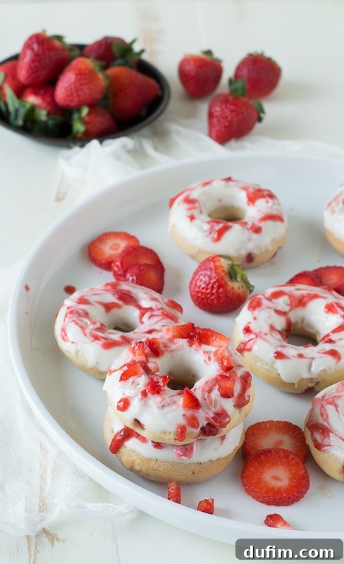 Strawberry Cheesecake Donut Delights 4 Several Strawberry Cheesecake Donuts artfully arranged on a white plate, highlighting the vibrant colors and appealing textures of the glaze and coulis.