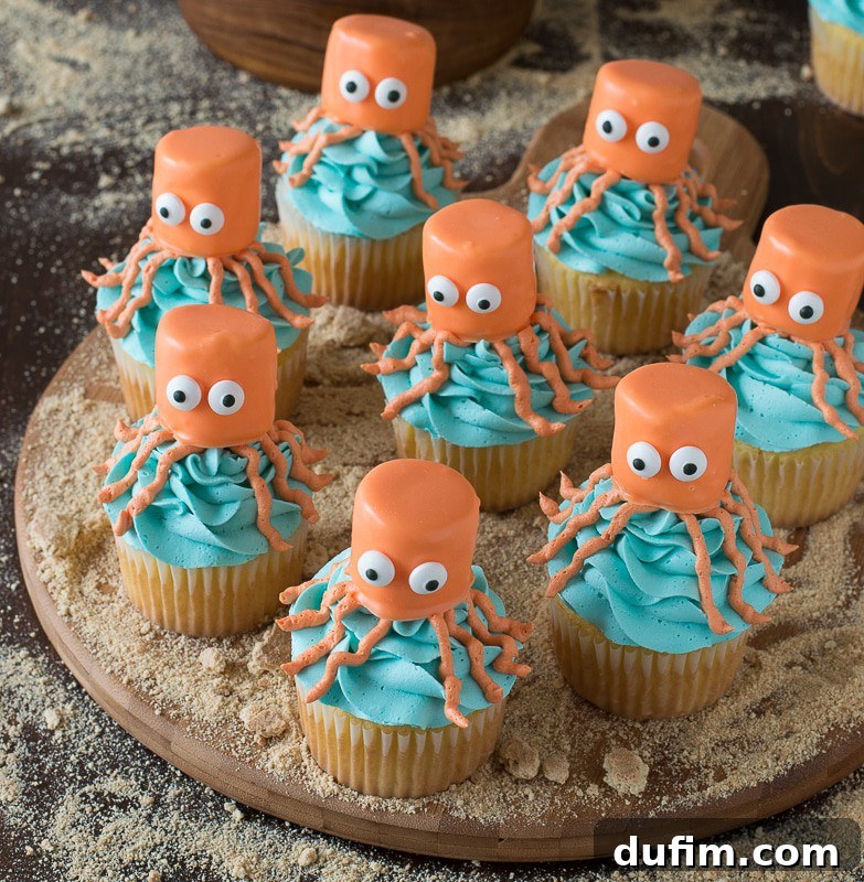Eight easy Octopus Cupcakes covered in vibrant blue buttercream frosting and topped with orange octopus bodies on a round wooden board.