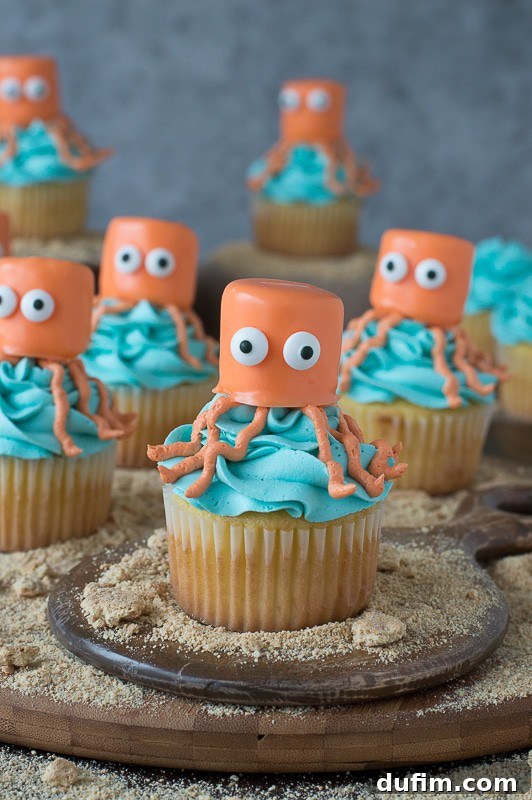 Seven easy vanilla Octopus Cupcakes covered in blue buttercream frosting on a round wooden board, showcasing their whimsical design.