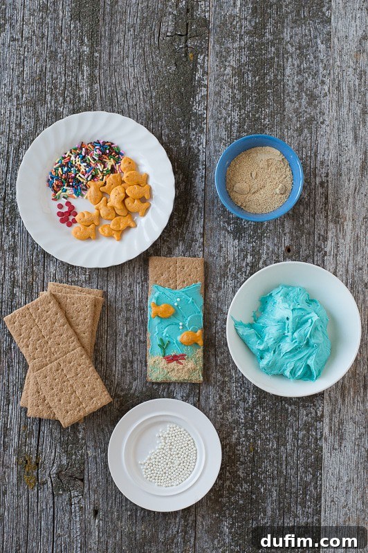 Under the Sea Graham Crackers - easy to make and perfect for an under the sea party! A charming flat lay of ingredients for Under the Sea Graham Crackers, featuring multi-colored sprinkles, a stack of golden graham crackers, and a bowl of creamy blue buttercream, all arranged on a warm wooden surface.