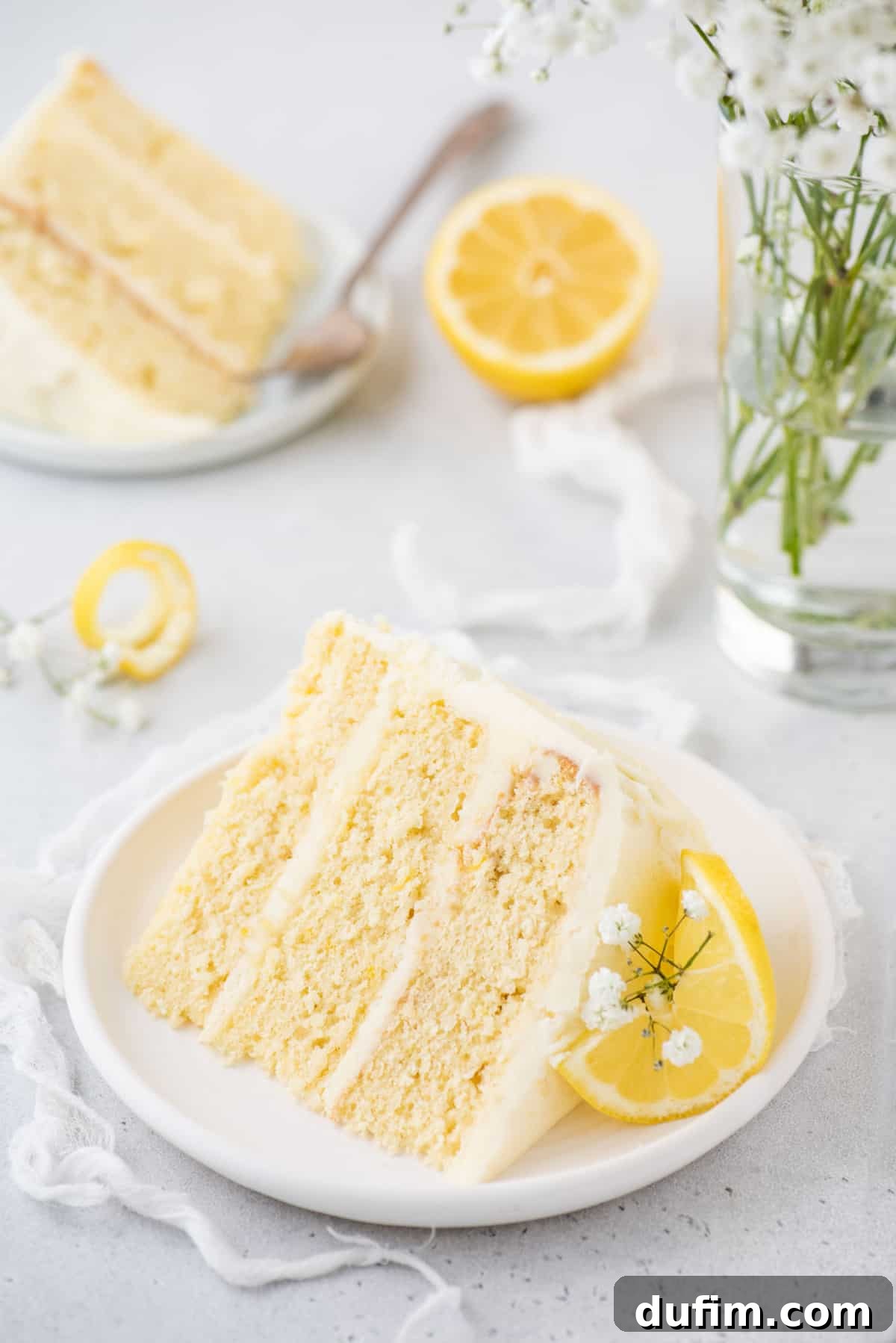 Two plates of three-layer lemon cake garnished with baby's breath and lemon slices, ready to be served.