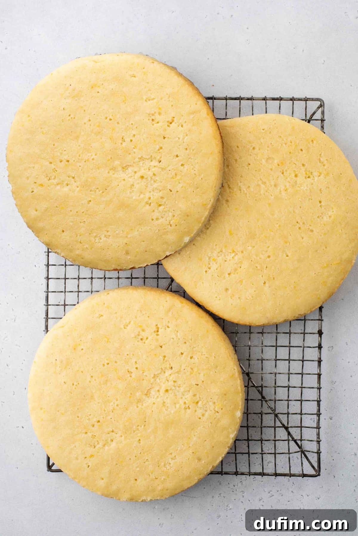 Three perfectly round lemon cake layers resting on a wire cooling rack, showcasing their even texture and golden crust.