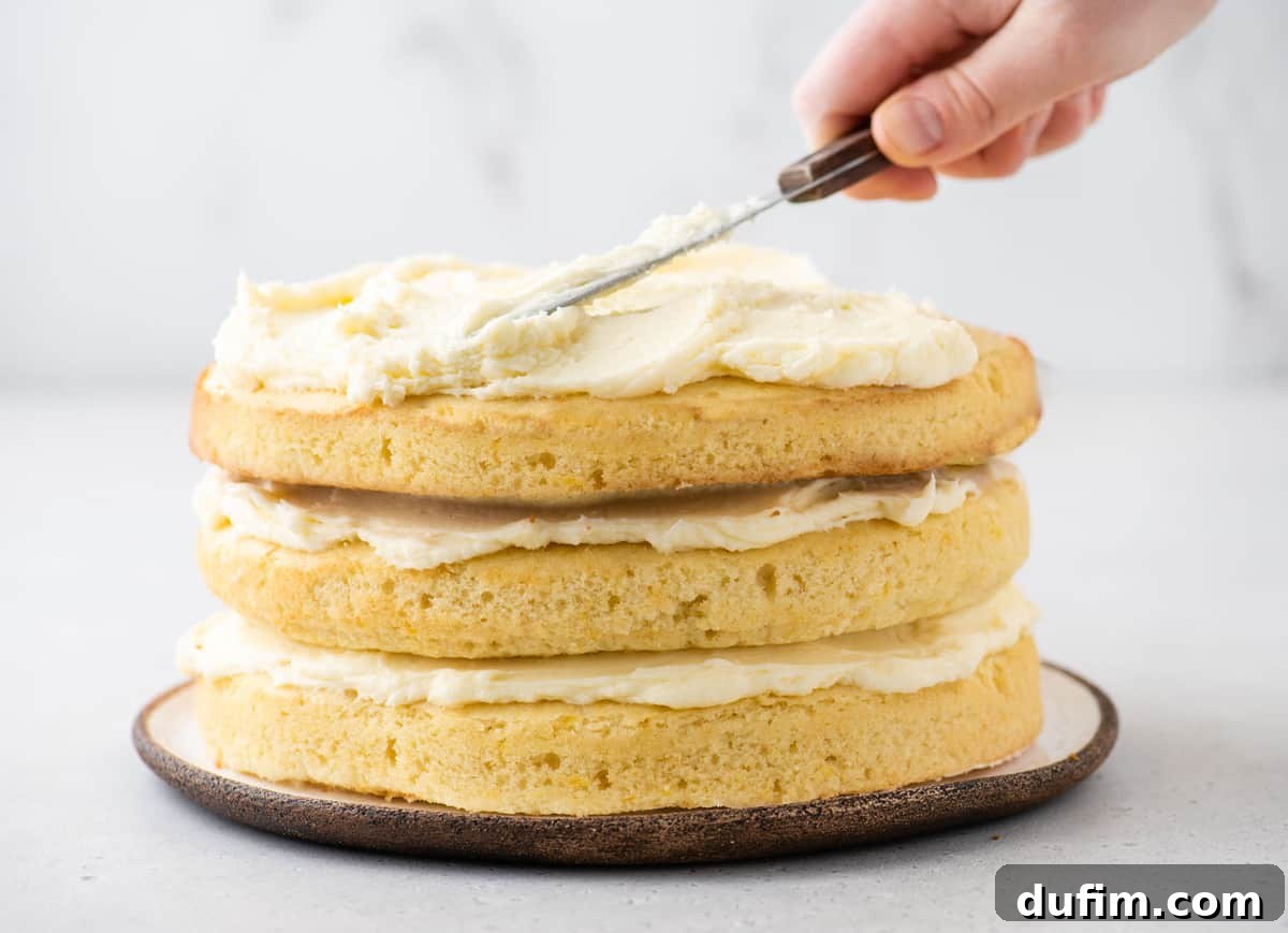 A baker expertly frosting the top of a three-layer lemon cake using an offset spatula, creating a smooth and professional finish.