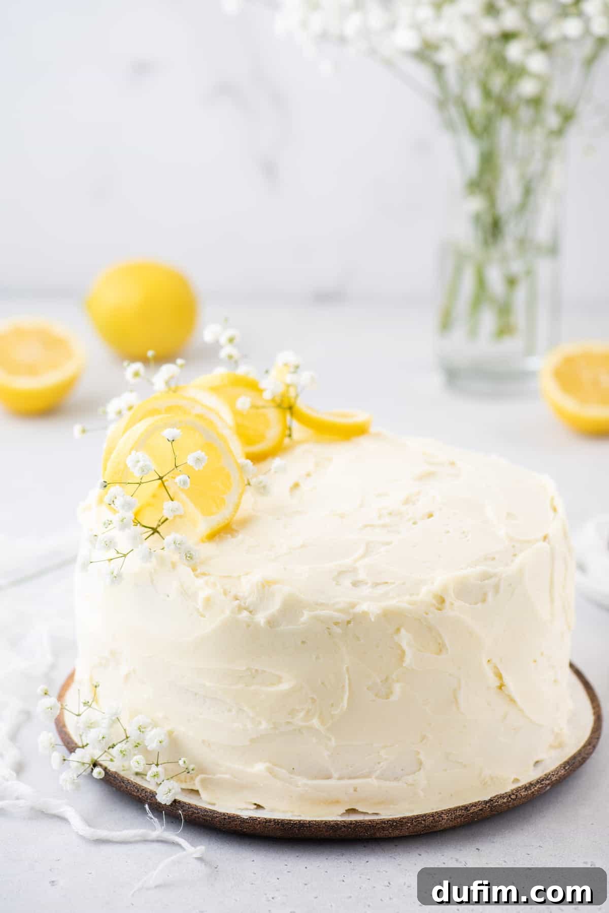 Whole lemon cake on a white cake stand, artfully garnished with delicate baby's breath flowers and fresh lemon slices.