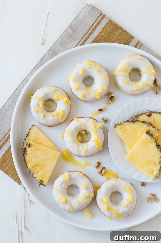 Lush Pineapple Walnut Donuts with a glistening white chocolate glaze and a vibrant pineapple puree drizzle, presented on a rustic board.