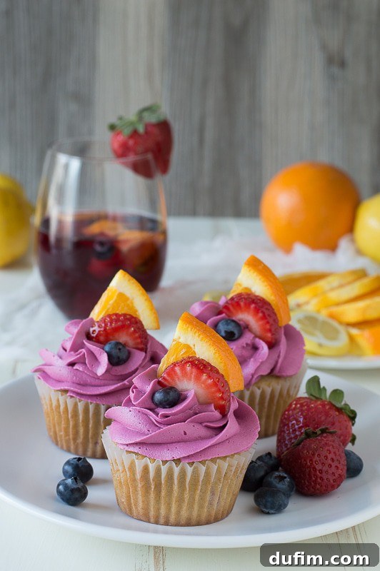 Beautifully frosted Sangria Cupcakes ready for a sweet escape Three Sangria Cupcakes with pink frosting surrounded by fresh strawberries and blueberries on a white serving plate. A close-up view highlighting the detailed frosting.