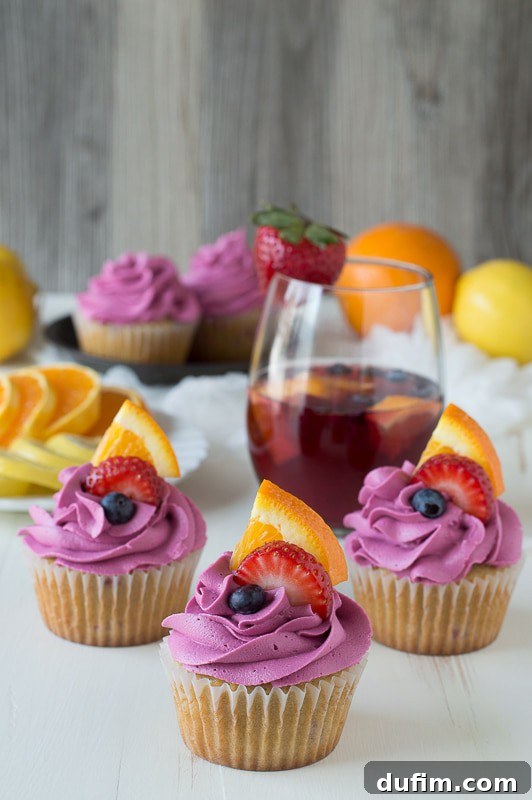 Garnished Sangria Cupcakes: a vibrant and elegant dessert Three delicious Sangria Cupcakes with red wine frosting and fresh blueberries, strawberries and sliced oranges. A close-up showing the rich details.