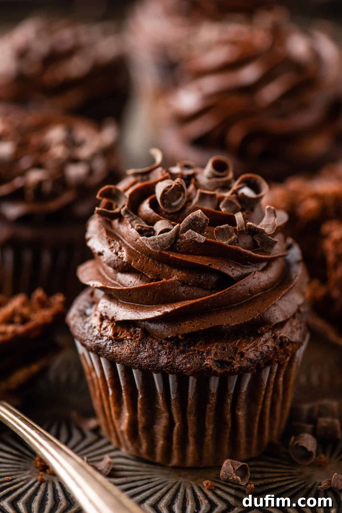 Decadent Chocolate Delights 2 chocolate cupcake with chocolate frosting on metal background with more cupcakes in the distance