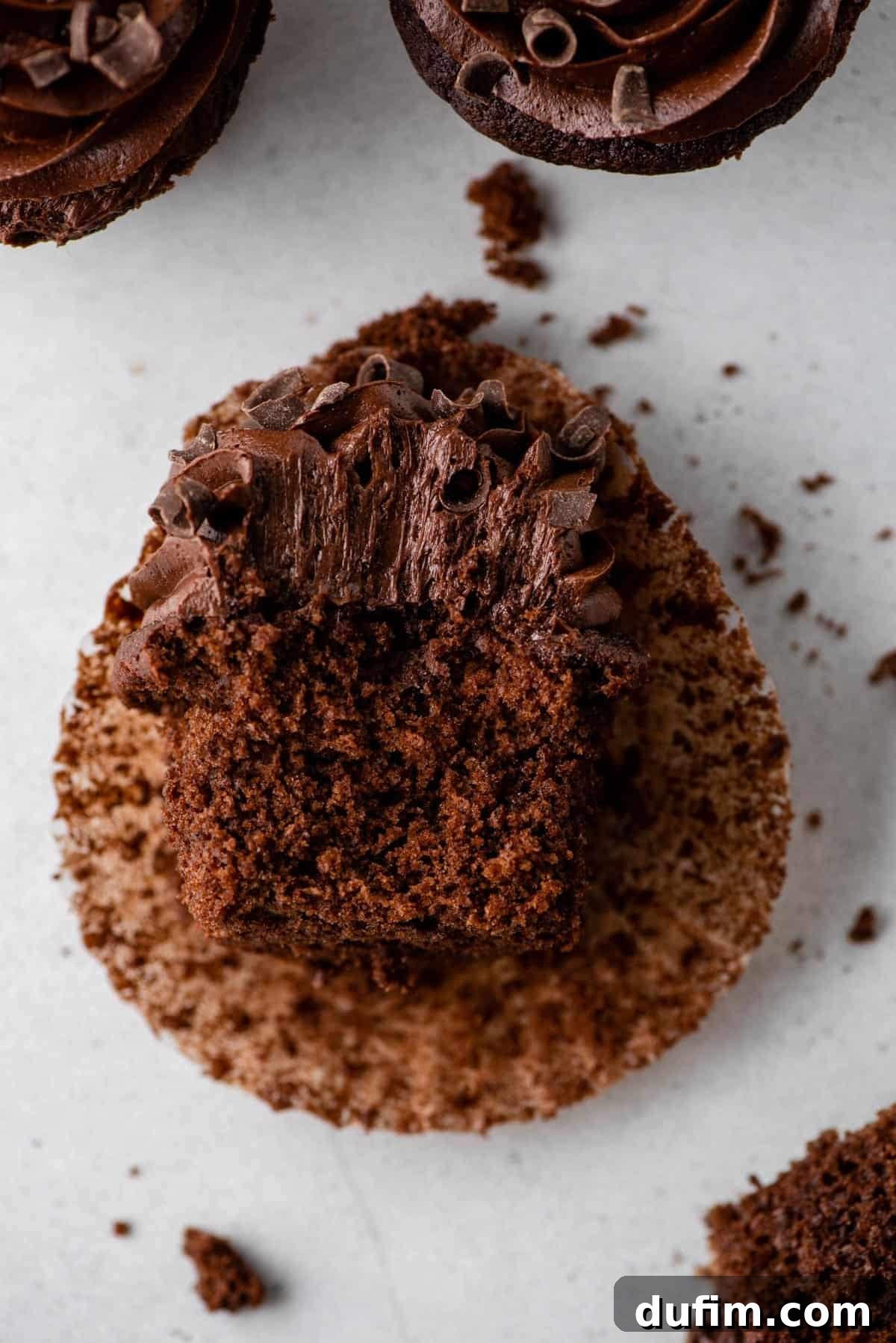 Decadent Chocolate Delights 3 chocolate cupcake laying on it’s side with a bite removed on gray background