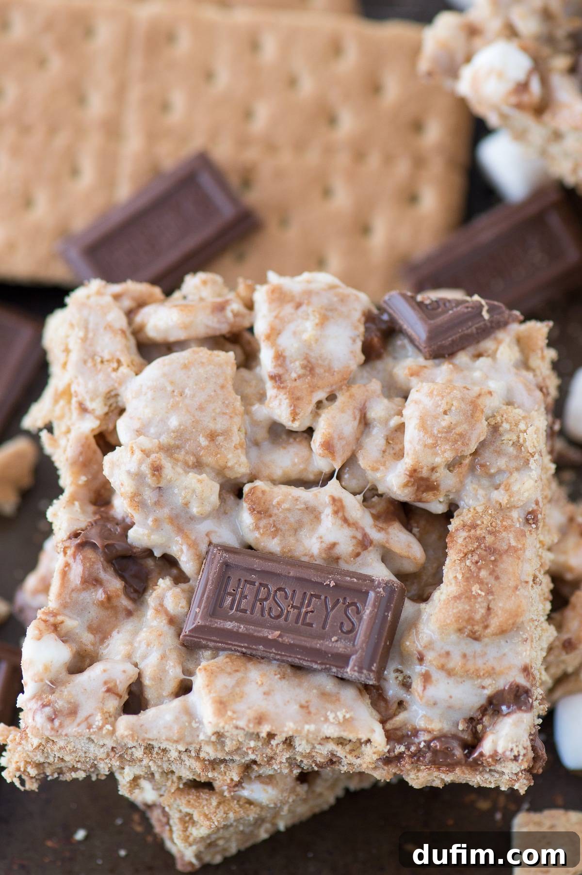 Stack of S'mores bars on a dark background, garnished with graham cracker pieces and Hershey's chocolate, emphasizing their rich and indulgent texture.