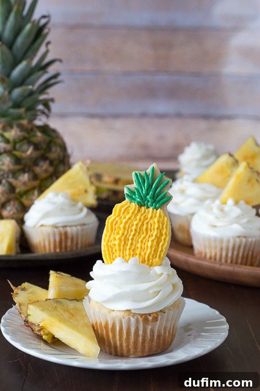 Pineapple Paradise Cupcakes 4 Three perfectly frosted pineapple cupcakes sit on a white platter, showcasing their delicate swirl of pineapple buttercream and inviting texture. One features a charming pineapple cookie on top.