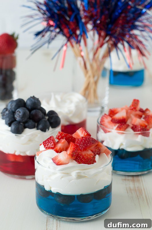 Vibrant blue jello in a clear glass cup, beautifully topped with a swirl of fluffy white whipped cream and a sprinkle of fresh, red chopped strawberries, creating a striking patriotic color contrast. This festive treat is ideal for summer celebrations.