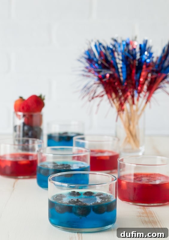A single clear glass cup featuring a vibrant blue jello layer, perfectly set and smooth, waiting for its whipped cream and berry toppings. The image highlights the clean, rich color of the jello against a pristine white background, showcasing its readiness for the next steps in creation.
