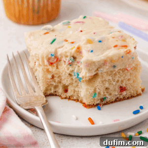 Effortlessly Light and Fluffy Funfetti Frosting 14 A slice of vanilla cake with colorful sprinkles and thick frosting sits on a white plate next to a fork. A few extra sprinkles are scattered on the plate.