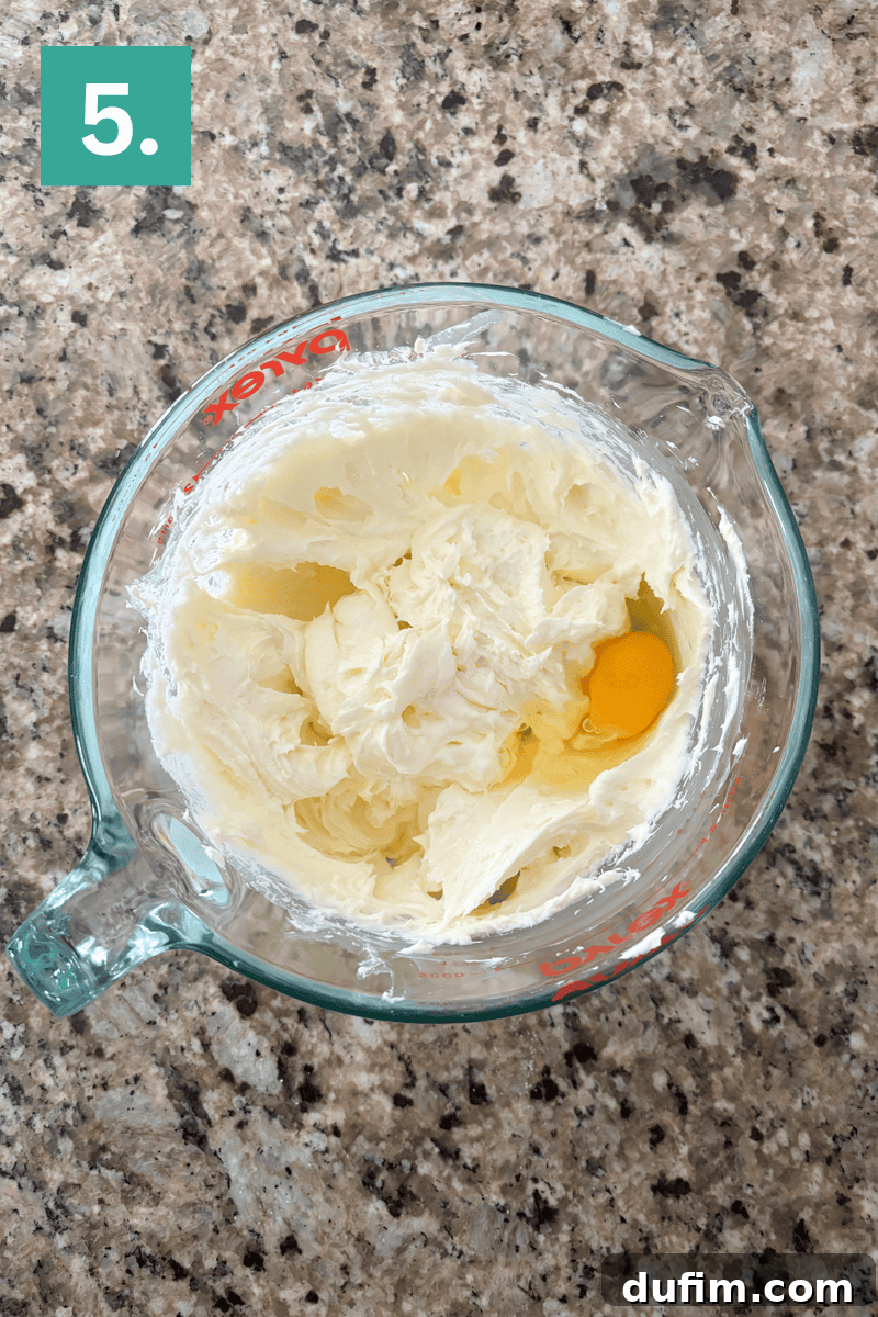 Creamed butter and sugar mixture in a glass bowl, with a whole egg carefully placed on top, ready to be beaten in.