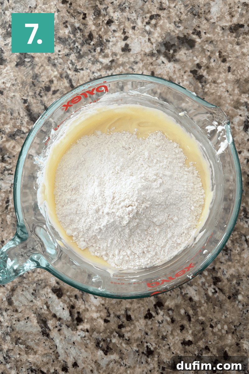 A glass measuring cup containing a partially mixed batter, showing traces of flour and wet ingredients before full integration.