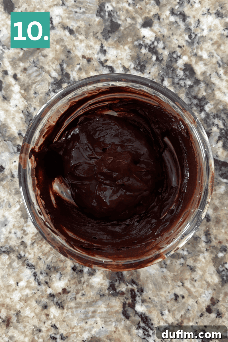 A glass bowl filled with rich, melted chocolate, smooth and glossy, awaiting its final use in the recipe.