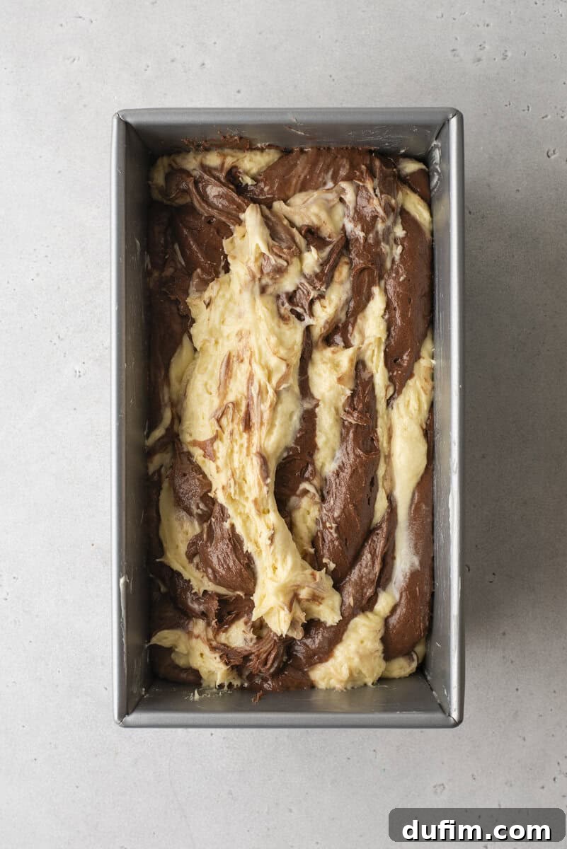 An unbaked marble cake batter in a loaf pan, showing distinct and beautiful swirls of chocolate and vanilla, ready for the oven.