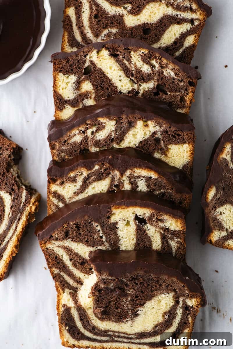 A beautifully sliced marble pound cake, showcasing intricate swirls of rich chocolate and creamy vanilla, is artfully arranged on parchment paper, its top covered with a luscious layer of chocolate glaze. A small, inviting dish of chocolate sauce sits nearby.