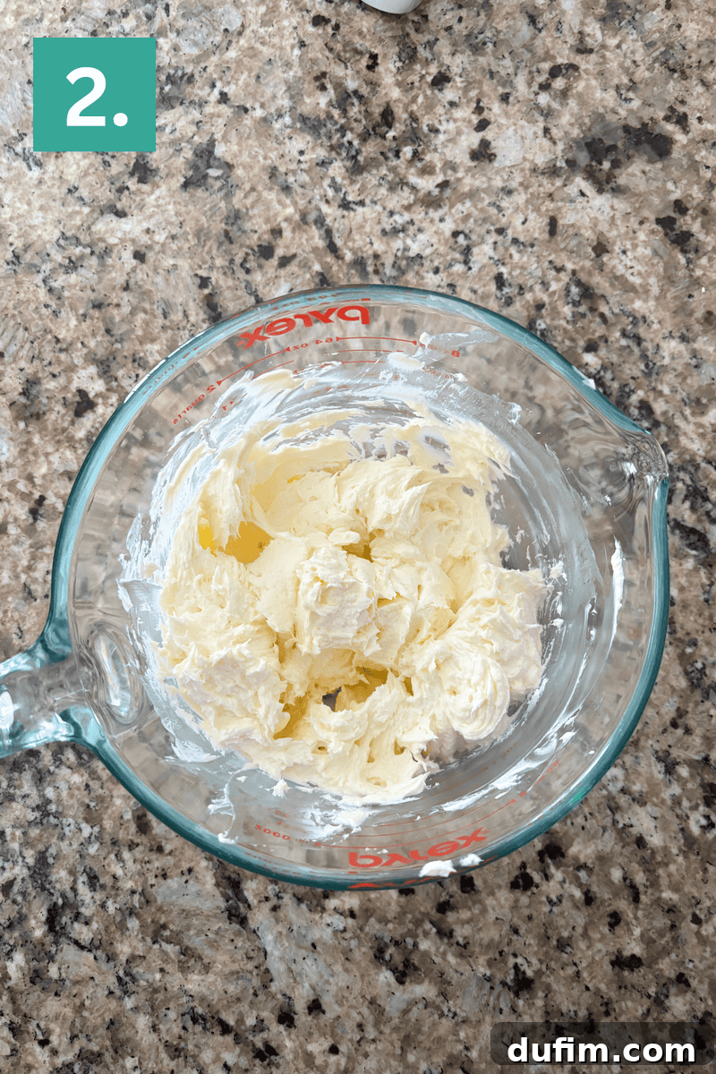 A creamy, whipped butter and cream cheese mixture in a glass bowl, light and fluffy after being beaten.