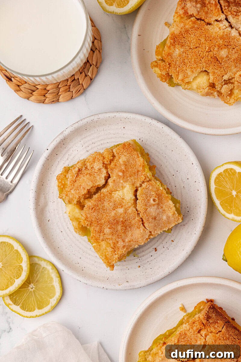 A pristine white plate holds a perfect square piece of lemon dessert bar, artfully positioned on a rustic wooden table. The scene is enhanced by scattering of fresh lemon slices, a tall glass of milk, and additional dessert bars neatly arranged on other plates. Two elegant forks rest nearby, inviting indulgence.
