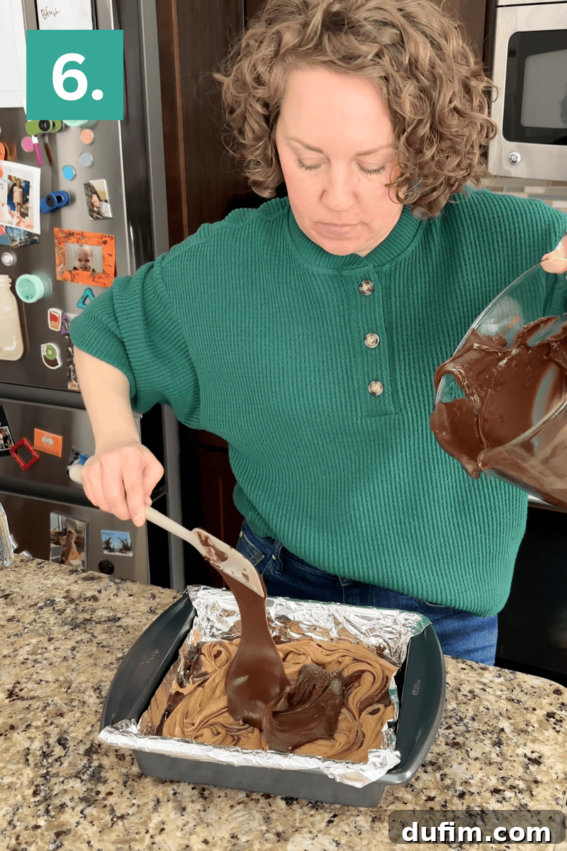 Decadent Chocolate Peanut Butter Fudge 11 A woman in a green sweater pours chocolate batter from a bowl into a foil-lined square baking pan on a granite countertop, following a recipe step labeled 6. Kitchen appliances and photos are visible in the background.