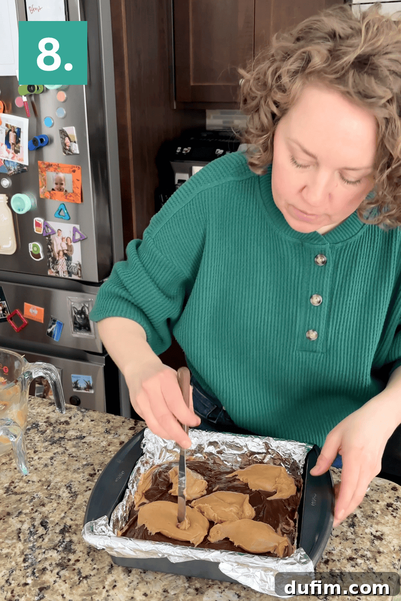 Decadent Chocolate Peanut Butter Fudge 13 A woman in a green sweater swirls peanut butter and chocolate in a foil-lined baking pan on a kitchen counter. A refrigerator with colorful magnets and photos is in the background. The number 8 is in the top left corner.
